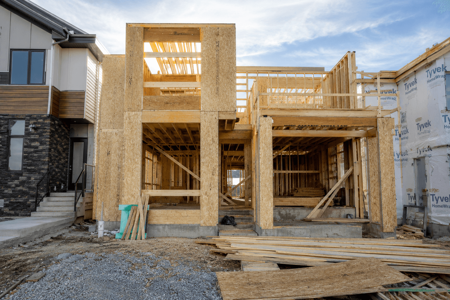 Wooden framing of a two-story house under construction between two other residential buildings.